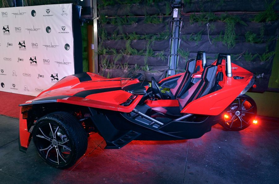 A red Polaris Slingshot sitting in front of a black and white background.