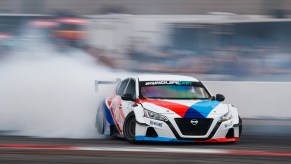 A 2021 widebody Nissan Altima shot while drifting as a large billowing cloud of tire smoke trails the vehicle. This car will be on display at SEMA 2021