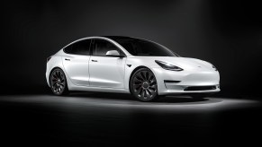 A white Tesla Model 3 facing toward the right in a black photo studio