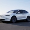 A white Tesla Model X driving on a road with the ocean in the background.