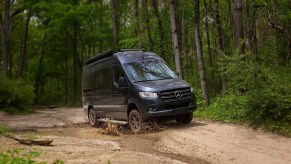 A dark-blue Thor Motor Coach Tranquility driving through a muddy forest