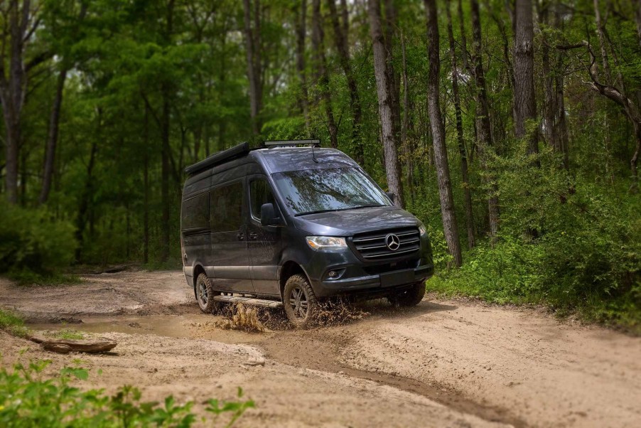 A dark-blue Thor Motor Coach Tranquility driving through a muddy forest