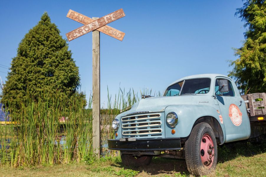 A weathered blue Studebaker 2R Series pickup truck by an overgrown railroad track