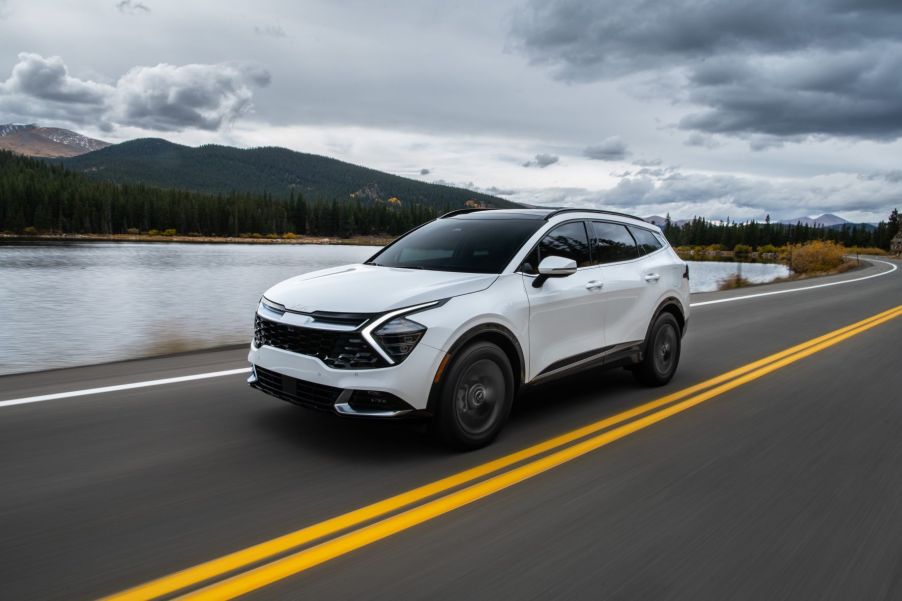 White 2023 Kia Sportage driving by a mountain lake