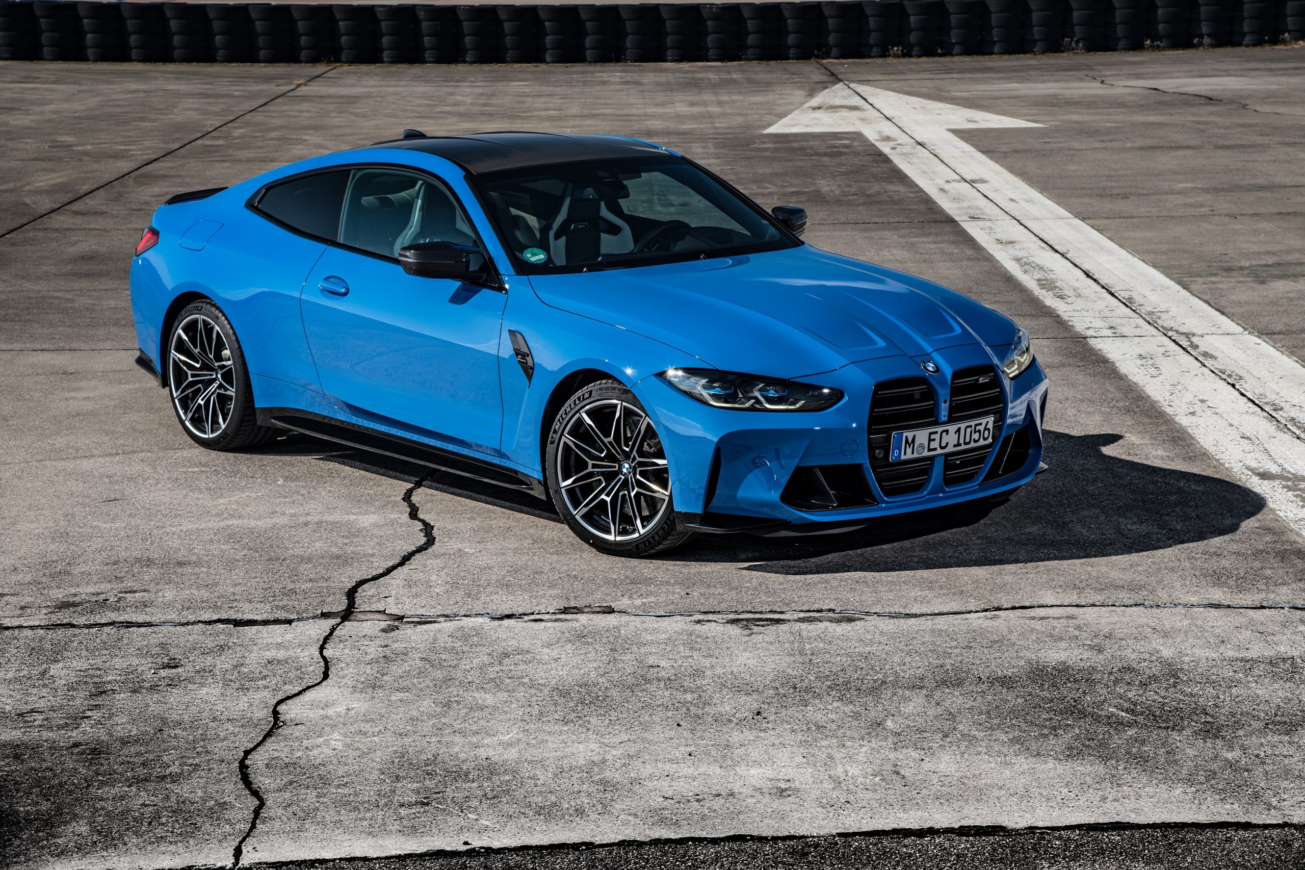 A blue BMW M4 shot from the front 3/4 on open tarmac