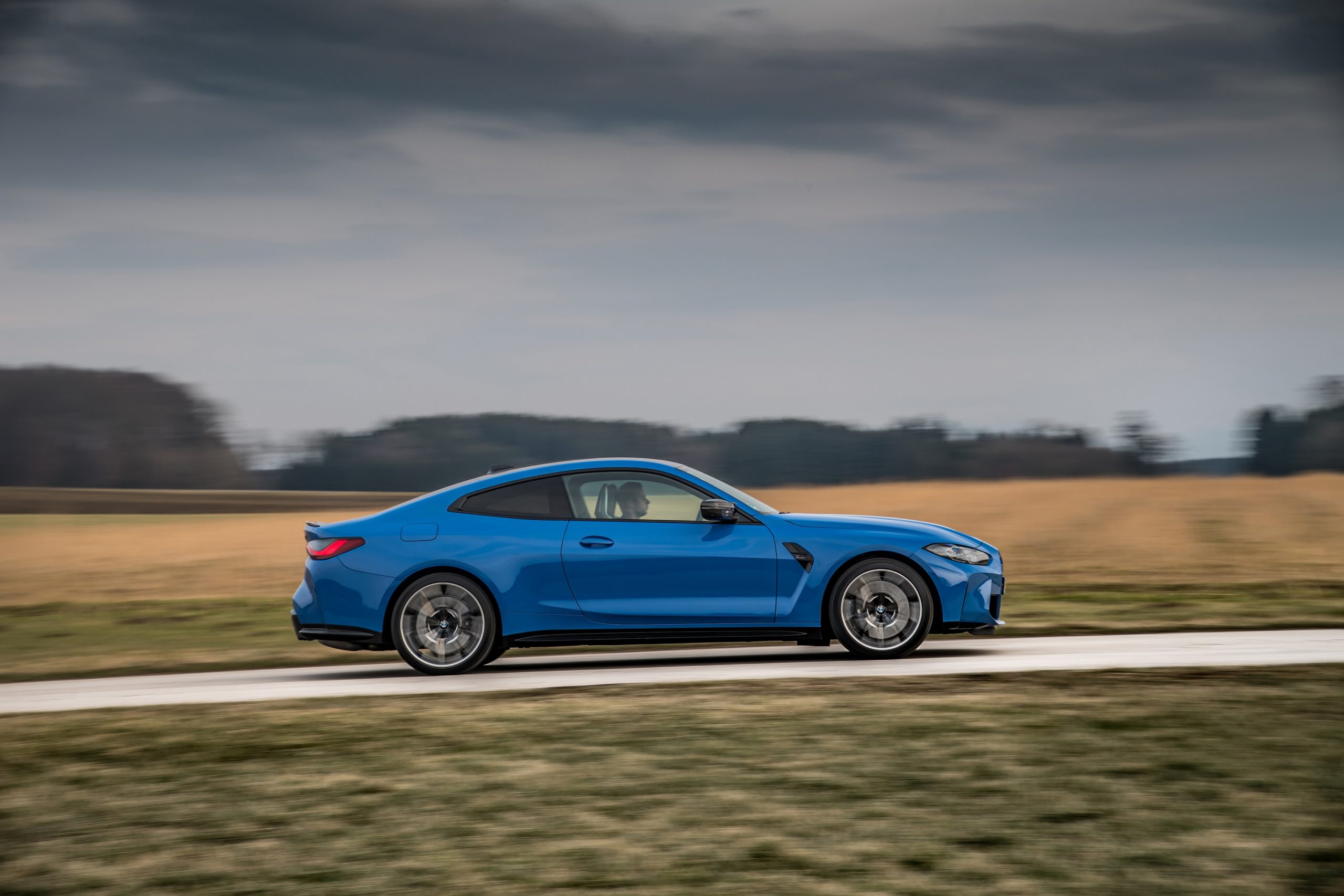 A blue BMW M4 shot in profile on a forested road