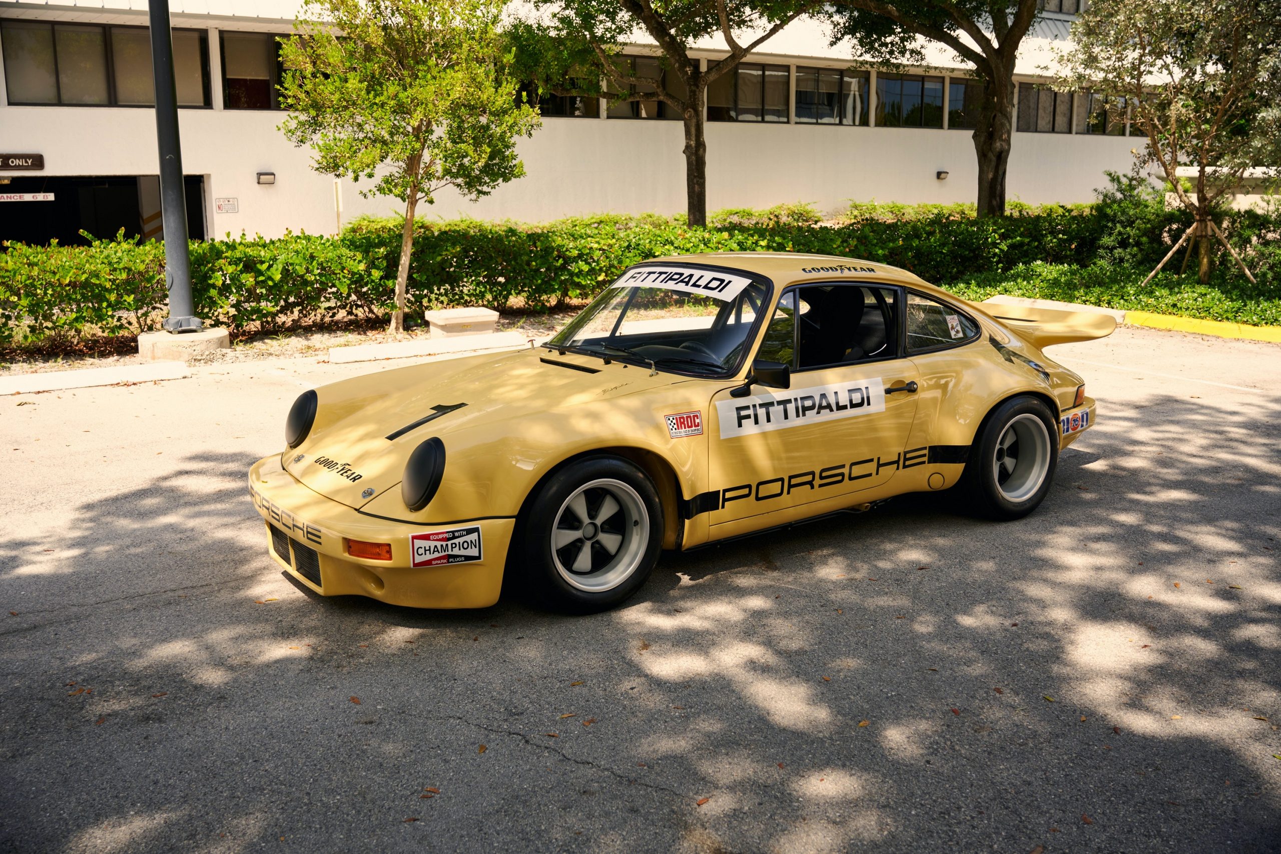 A yellow Porsche 911 RSR race car, shot from the far 3/4 angle in the shade