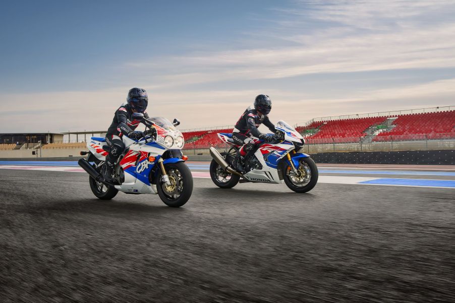 Two black-clad riders on white-red-and-blue 1992 Honda CBR900RR Fireblade next to a 2022 Honda CBR1000RR-R Fireblade SP 30th Anniversary Edition motorcycles