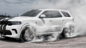 The 2021 Dodge Durango SRT Hellcat muscle three-row SUV in white with a hood vent and stripes as tires spin and generate smoke