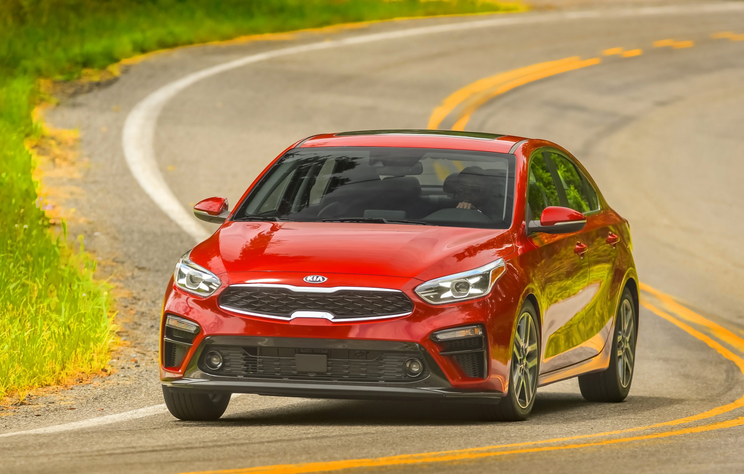 A red 2021 Kia Forte compact sedan shot from the 3/4 angle on a back road