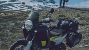 A black-silver-and-green 2022 Husqvarna Norden 901 with accessory bags parked on an alpine country road