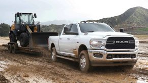 A white 2022 Ram 2500 heavy-duty pickup truck tows a trailer carrying a bulldozer through mud.