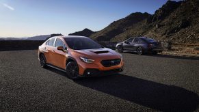 An orange 2022 Subaru WRX shot in the foreground from the 3/4 angle with a blue model behind