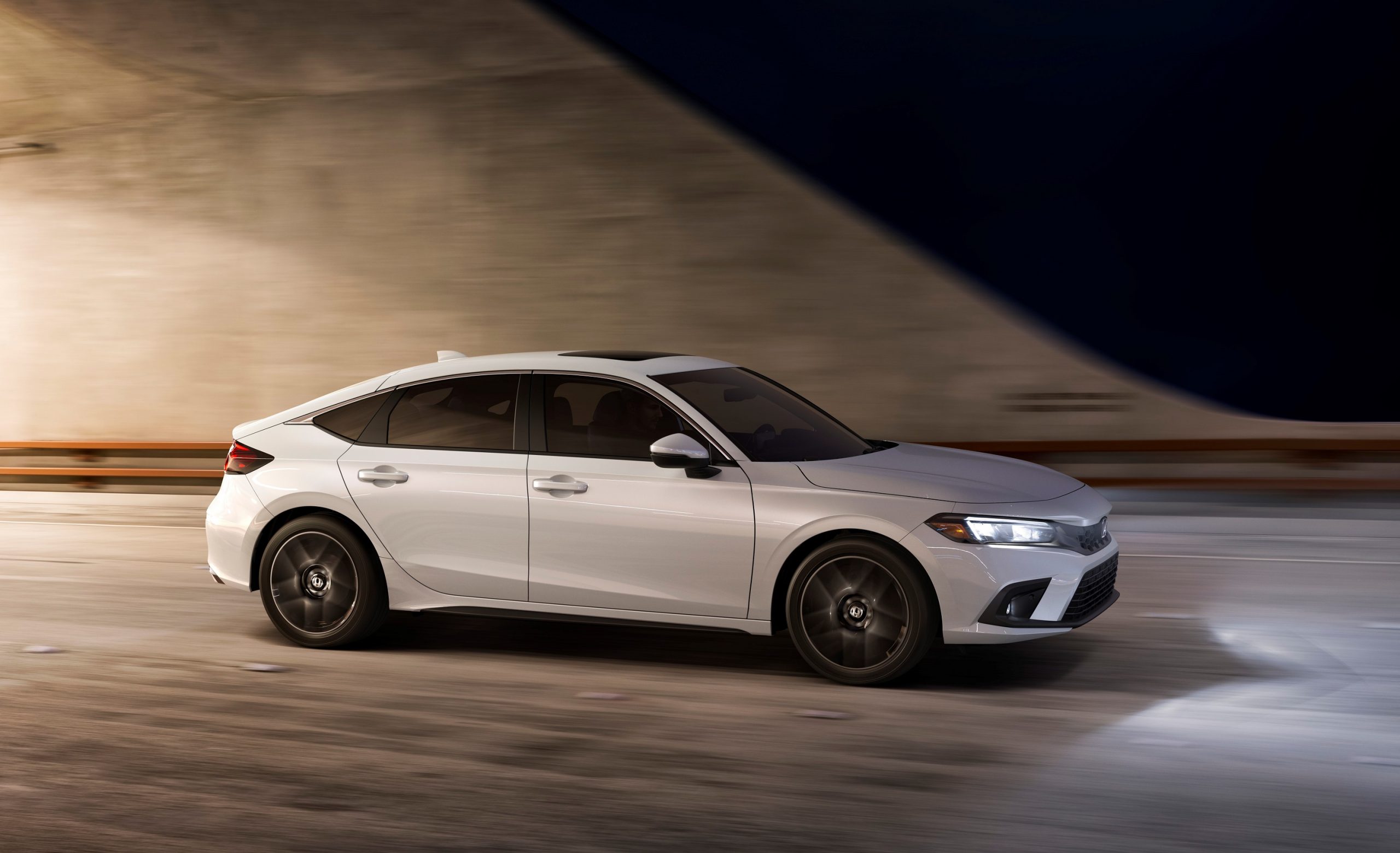 A white 2022 Honda Civic hatchback shot in profile on a highway at night