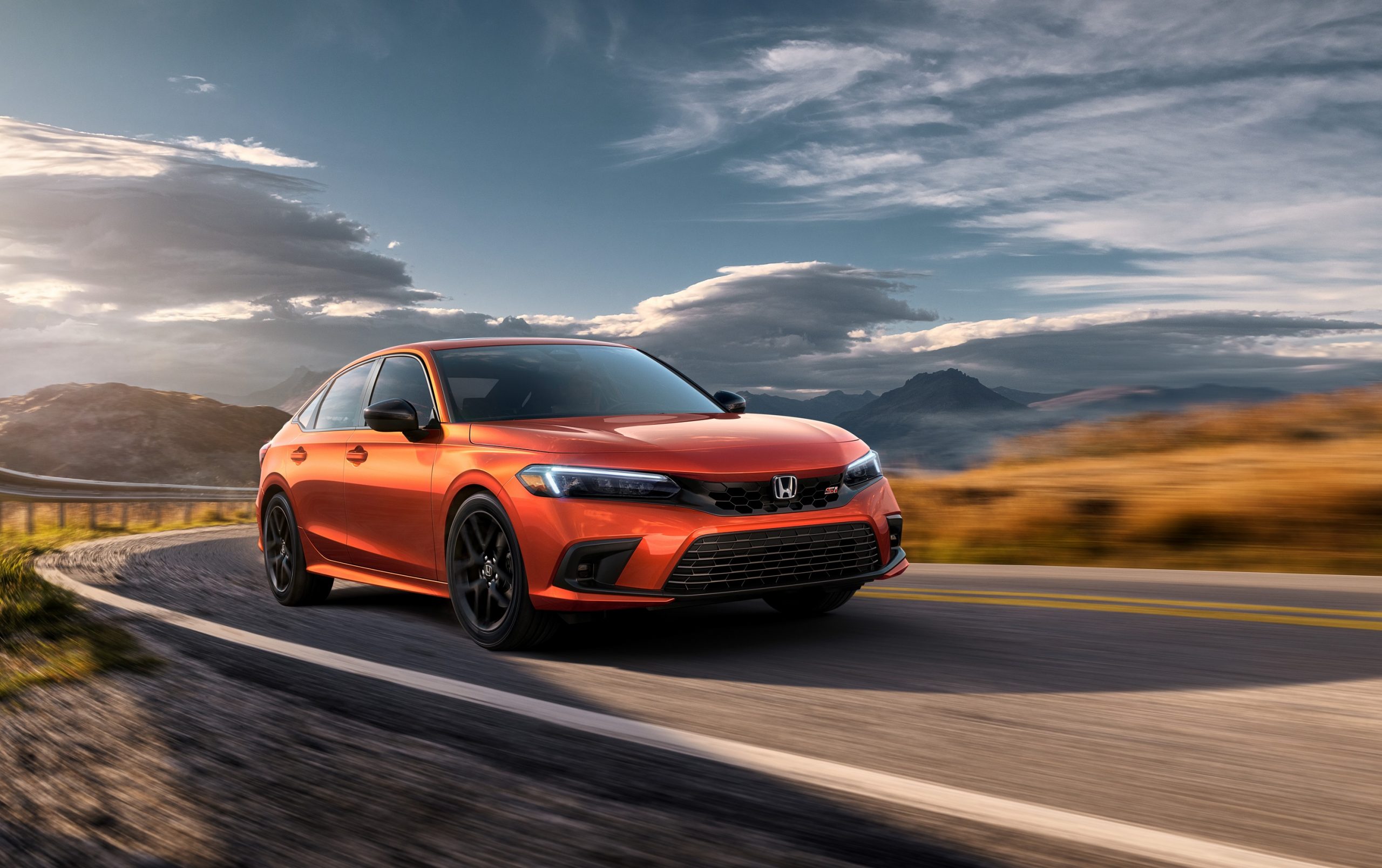 An orange 2022 Honda Civic Si shot from the front 3/4 on a back road