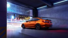 An orange 2022 Honda Civic Si, shot from the rear in a garage at night