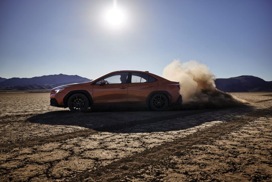 An orange non-JDM 2022 Subaru WRX sports sedan mid-drift on a desert lakebed