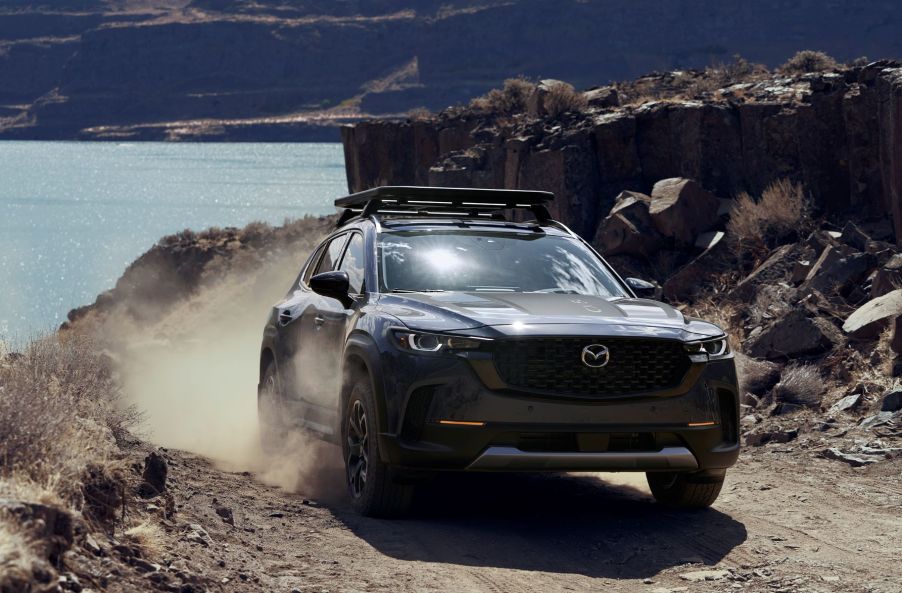 Zircon Sand 2023 Mazda CX-50 driving on a rocky road near a lake