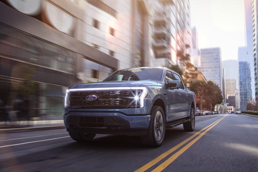 Blue 2022 Ford F-150 Lightning driving down the street, ready to charge battery at EV charging station