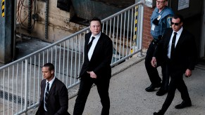 Elon Musk leaving a court room surrounded by security. Musk may be called as a witness in an upcoming Tesla crash trial