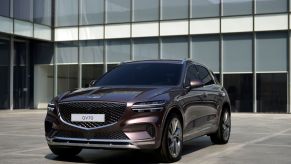 The Genesis GV70 luxury compact crossover SUV with a dark red paint color option parked on a building's entrance plaza