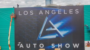 A massive vinyl sign for the LA Auto Show being hoisted onto the LA Convention Center