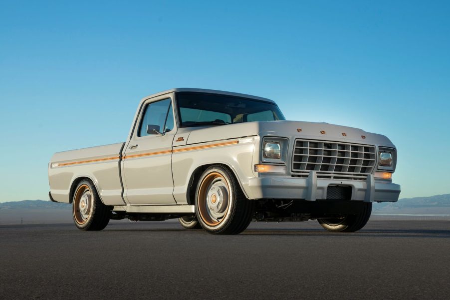 Passenger's side front angle view of grey and orange Ford F-100 EV pickup truck at SEMA 2021