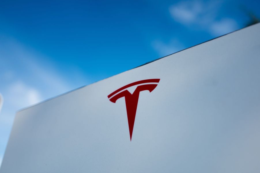 A red Tesla logo on a white building with a blue sky.