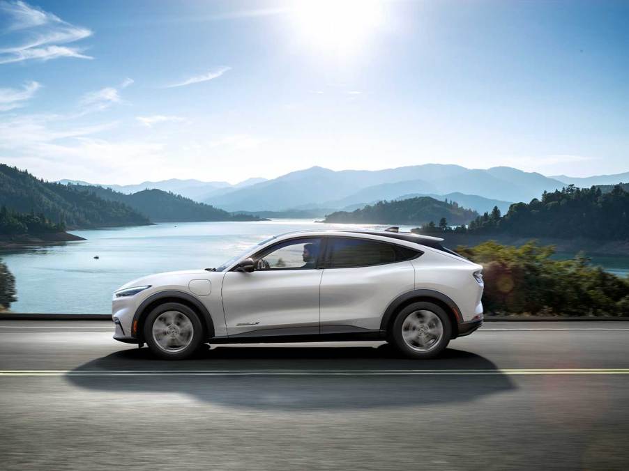 White 2022 Ford Mustang Mach-E crossover EV driving by a mountain lake