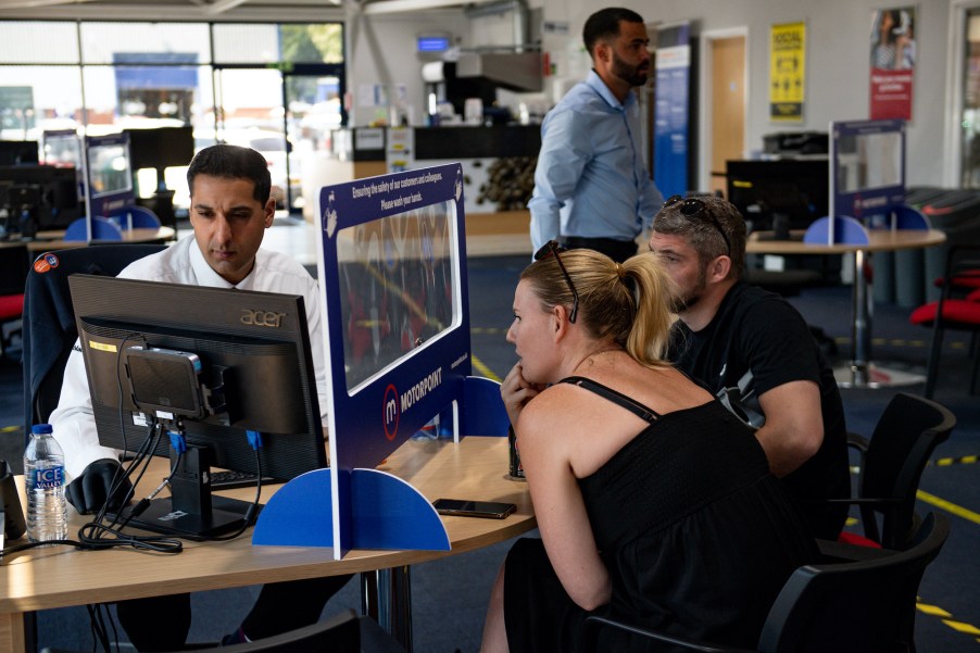 A car salesman talks to a customer from behind a screen