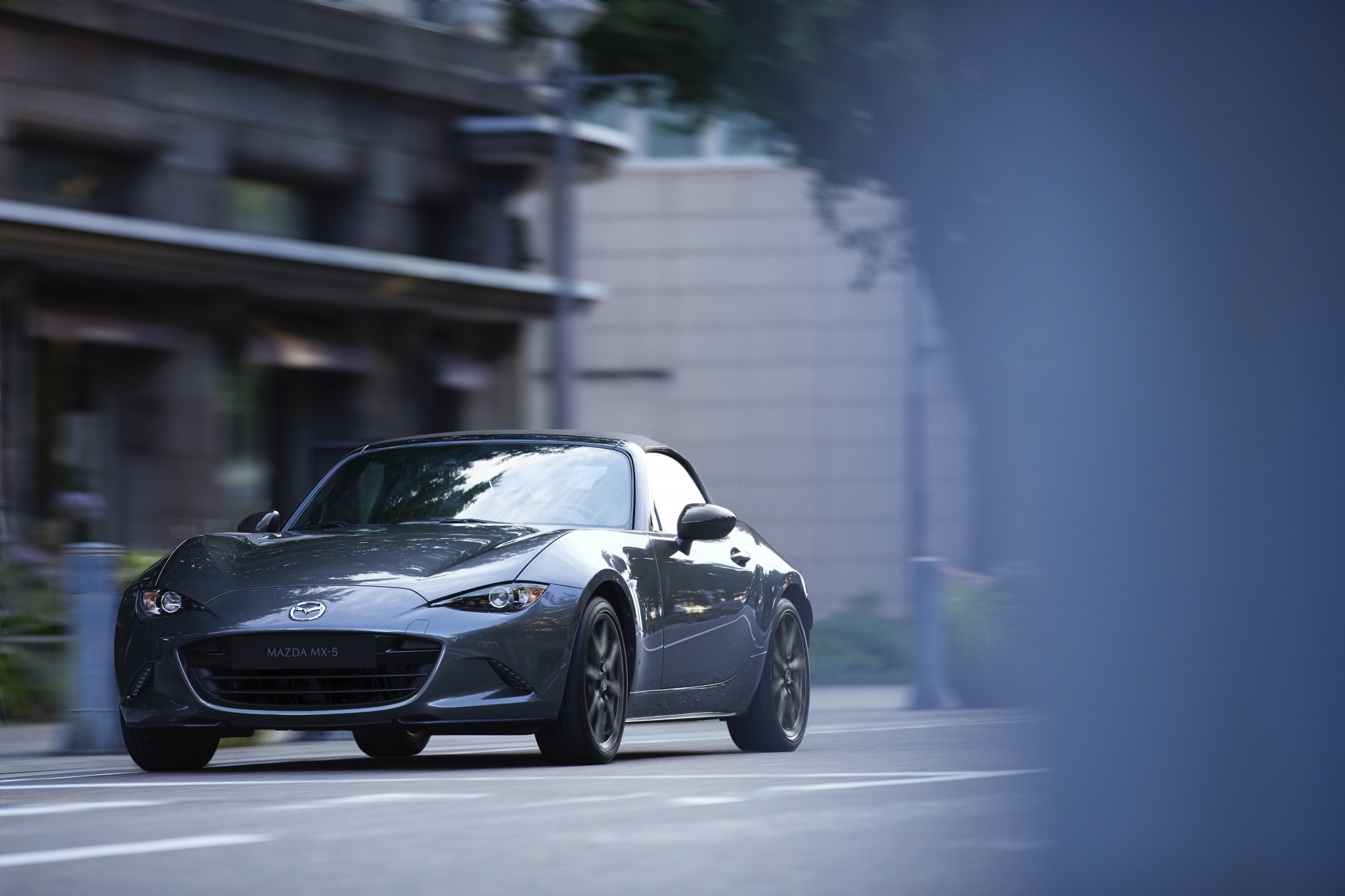 A grey Miata convertible shot from the front 3/4 on a city street