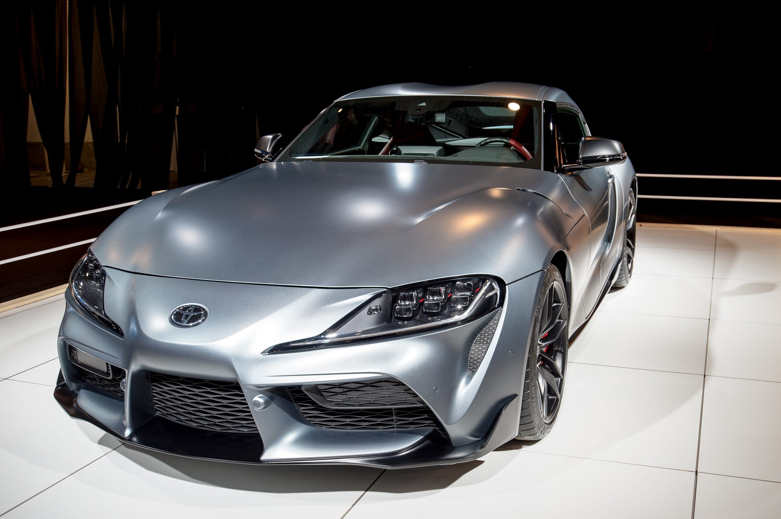 A matte grey Toyota Supra with a BMW-derived engine shot from the 3/4 angle at an auto show