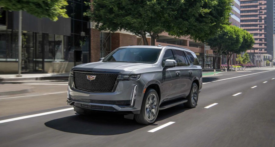 A gray 2022 Cadillac Escalade drives along a road during the day with buildings in the background.