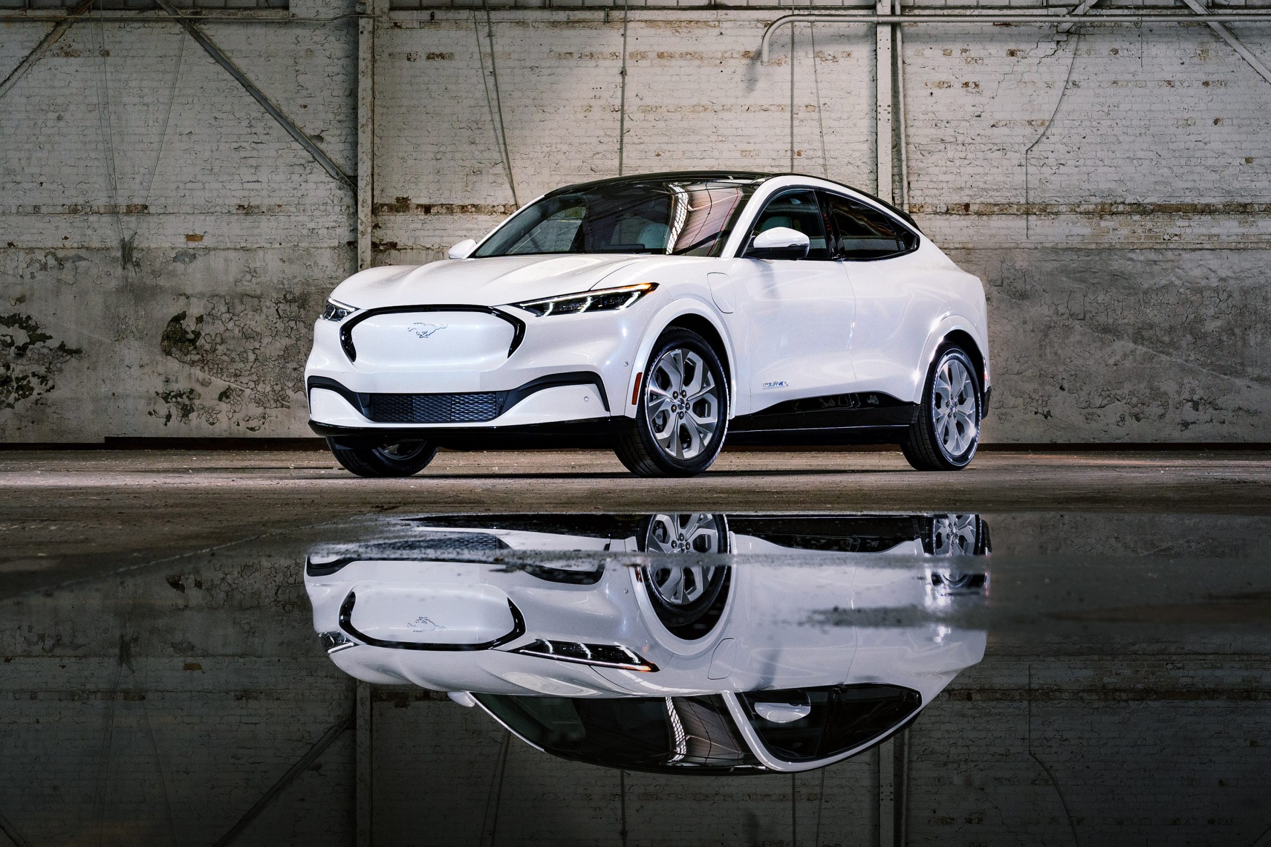 A white 2022 Ford Mustang Mach E EV shot from the front 3/4 with the vehicle reflecting in a puddle in the foreground