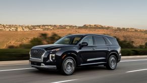 A 2022 Hyundai Palisade midsize crossover SUV driving down a highway with homes on grassy hills in the background