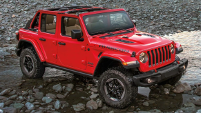 A 2022 Jeep Wrangler Rubicon compact off-road SUV with the Firecracker Red paint color option parked on a trail of water, mud, and rocks