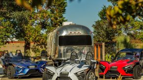 A blue 2022 Polaris Slingshot R next to a white 2022 SL next to an accessorized red 2022 S in front of an Airstream trailer