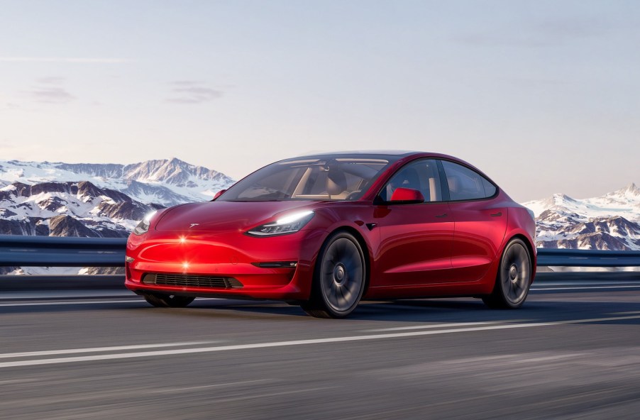 A fully loaded new Red Multi-Coat 2022 Tesla Model 3 driving by snowy mountains