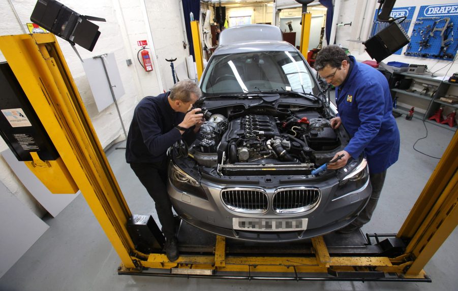 Two men work on a BMW sedan in a shop