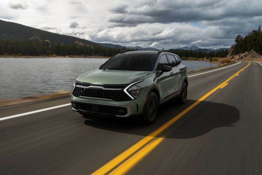 Green 2023 Kia Sportage driving by a mountain lake