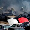 A depiction of a junkyard fire with firefighters and cars.