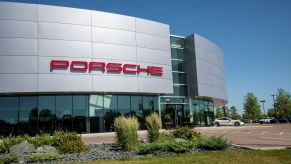 White Porsche dealership with Porsche written in red on the outside with grass and shrubbery.