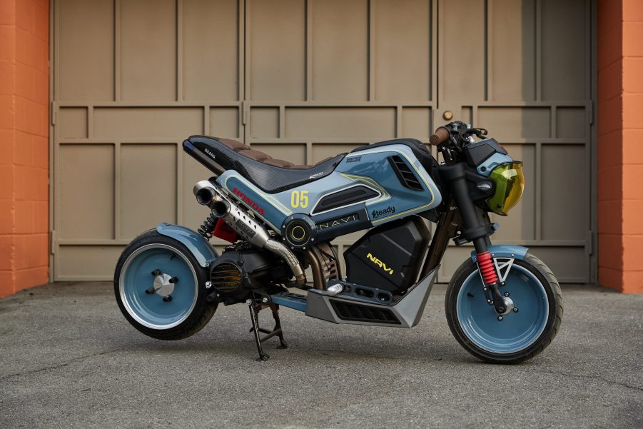 The blue-black-and-yellow Steady Garage 'Project Naviscape' custom 2022 Honda Navi next to a garage