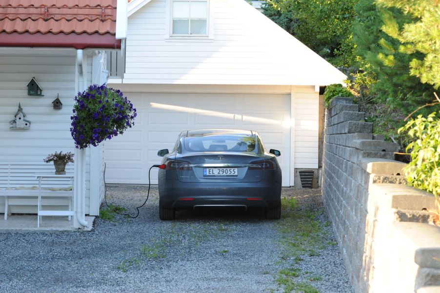 A grey Tesla charging in front a white residential home.