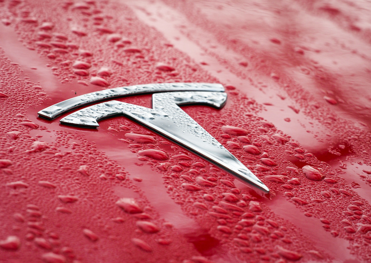 The Tesla logo on the wet hood of a red passenger car