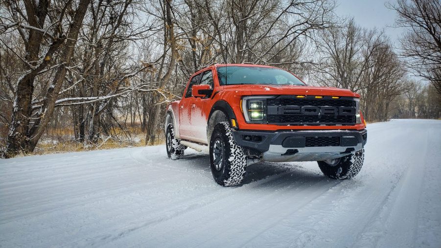 An orange 2021 Ford Raptor truck shot from the front 3/4 during a snow storm