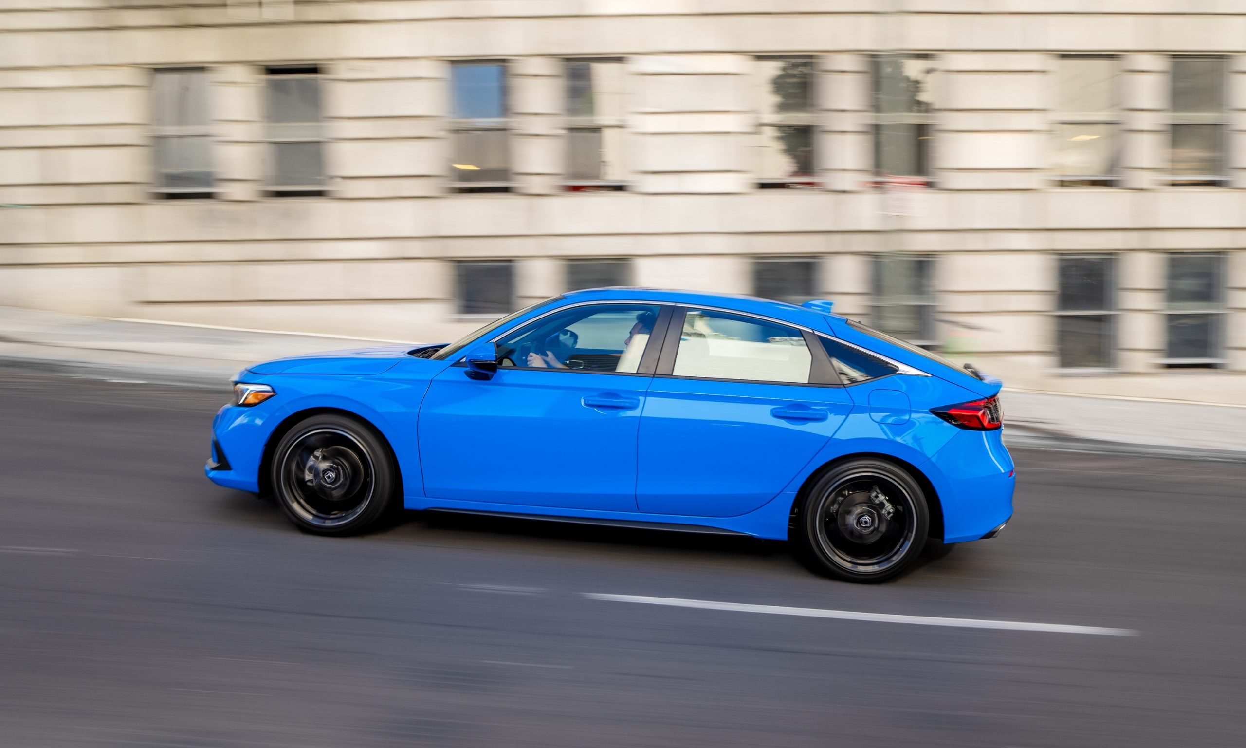 A blue Civic hatchback shot in profile on a city street