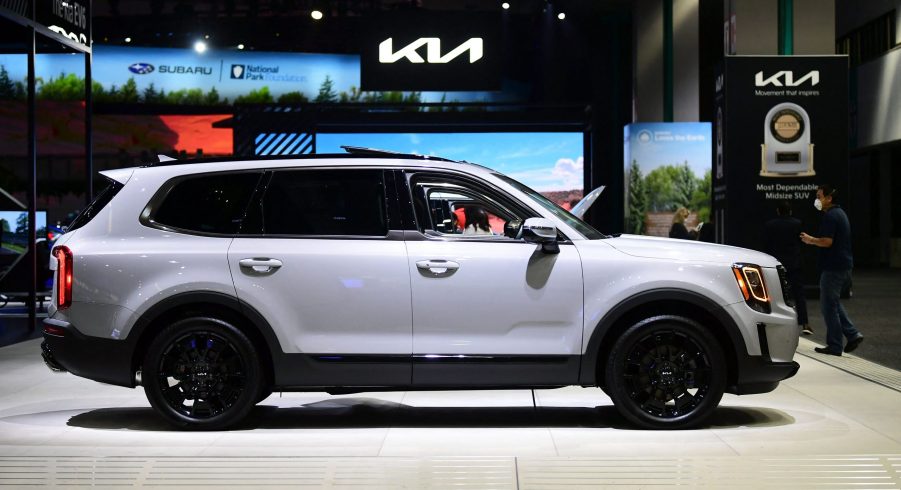 A white 2022 Kia Telluride in a building with the Kia logo in the background above the car.