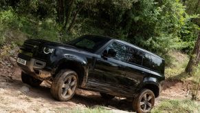 2022 Land Rover Defender 110 luxury off-road SUV riving on a rocky dirt trail in a forest