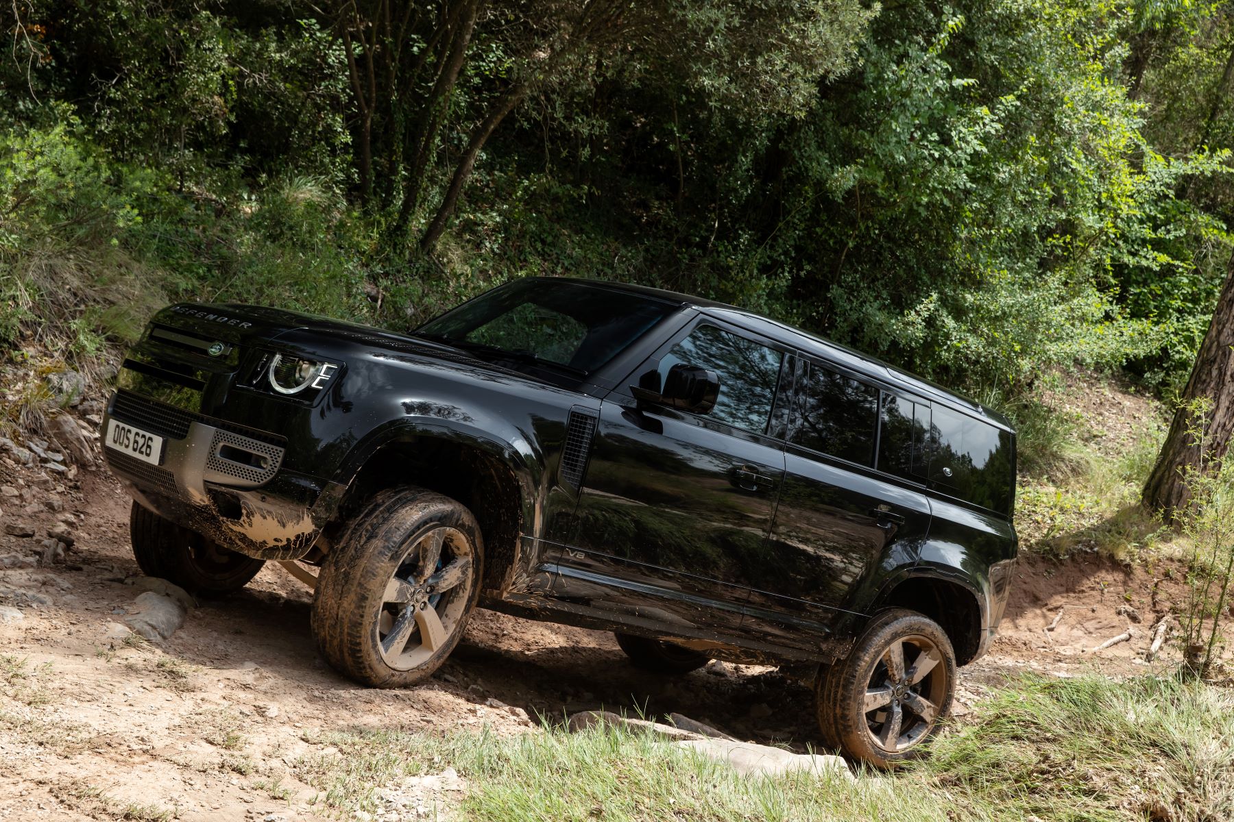 2022 Land Rover Defender 110 luxury off-road SUV riving on a rocky dirt trail in a forest